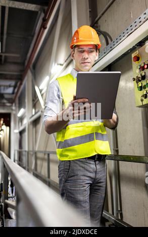 Lavoratore in abiti riflettenti utilizzando un tablet PC da ringhiera in magazzino Foto Stock
