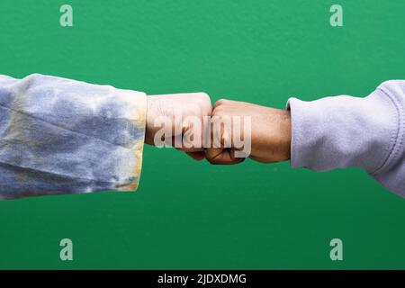 Mani di amici che battono i pugni di fronte al muro verde Foto Stock