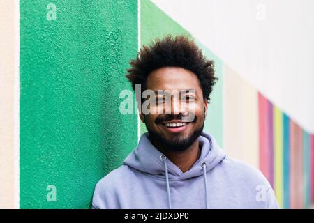 Sorridente afroista appoggiato su una parete colorata Foto Stock