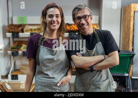 Sorridenti proprietari di negozi che indossano grembiuli in piedi nel mercato biologico Foto Stock