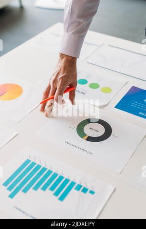 Mano di uomo d'affari con penna che analizza grafici e grafici alla scrivania in ufficio Foto Stock