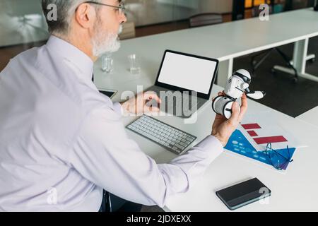 Uomo d'affari che analizza robot giocattolo seduto alla scrivania in ufficio Foto Stock