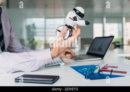 Mano di uomo d'affari che tiene robot giocattolo seduto alla scrivania in ufficio Foto Stock