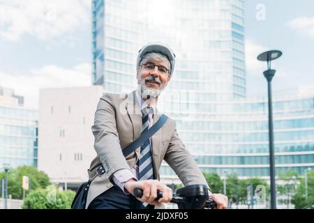 Felice uomo d'affari con scooter elettrico a spinta di fronte agli edifici di uffici Foto Stock