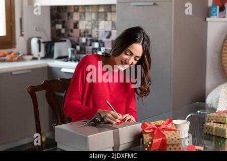 Donna sorridente che scrive sul contrassegno del regalo per regalo di Natale nel paese Foto Stock