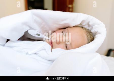 Ragazza malata avvolta in coperta con termometro a letto a casa Foto Stock