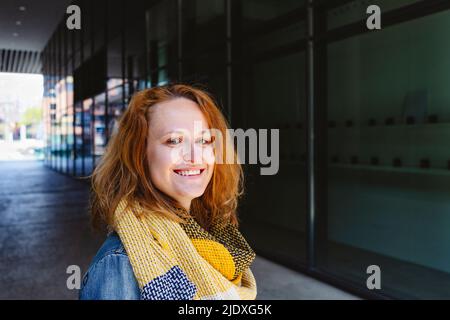 Donna felice con sciarpa gialla in plaid in piedi in galleria Foto Stock