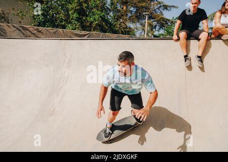 Uomo skateboard sulla rampa sportiva con gli amici in background Foto Stock