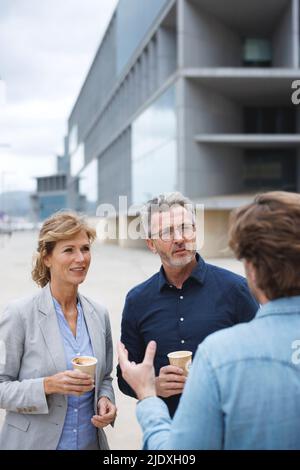 Uomo d'affari che discute con i colleghi che tengono le tazze di caffè usa e getta Foto Stock