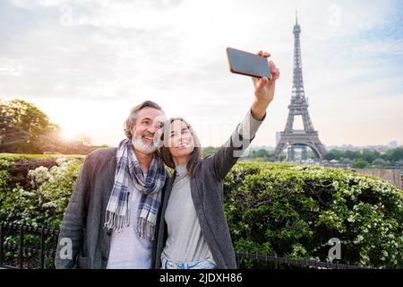 Donna felice che prende selfie con l'uomo attraverso lo smartphone di fronte alla Torre Eiffel, Parigi, Francia Foto Stock