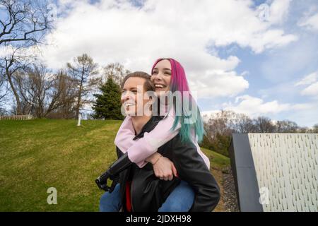 Buon giovane uomo che dà giro piggyback alla ragazza con i capelli tinti Foto Stock