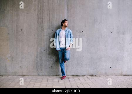 Uomo che guarda via appoggiandosi su una parete grigia Foto Stock