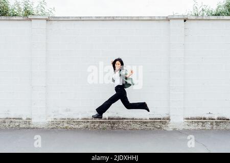 Donna felice che salta di fronte al muro Foto Stock