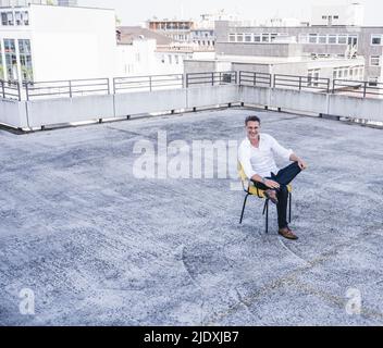 Uomo d'affari maturo sorridente seduto sulla terrazza dell'edificio Foto Stock