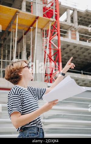 Sorridente architetto che sostiene il progetto che punta al cantiere Foto Stock