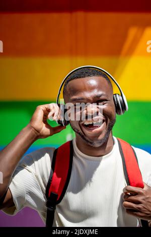 Uomo felice con cuffie wireless di fronte alla parete dell'arcobaleno Foto Stock