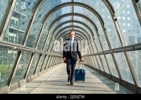 Uomo d'affari maturo con valigia che cammina sul ponte pedonale Foto Stock
