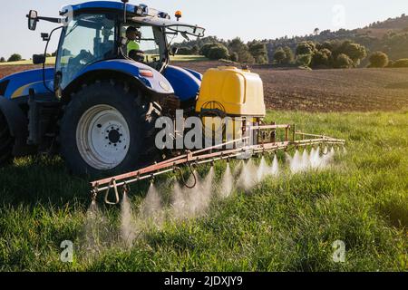 L'agricoltore spruzza il fertilizzante attraverso l'irroratrice che si trova nel trattore su campo Foto Stock