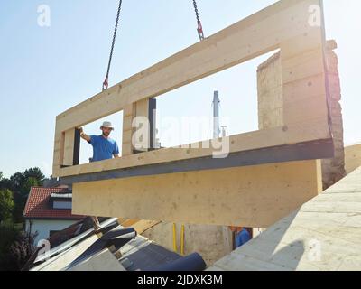 Lavoratori che installano telaio in legno sulla parte superiore della casa con gru Foto Stock