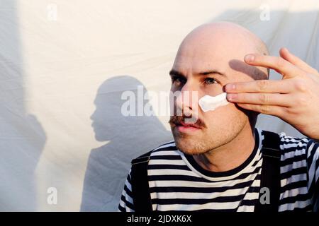 Calvo uomo che applica moisturizer di fronte a sfondo bianco Foto Stock