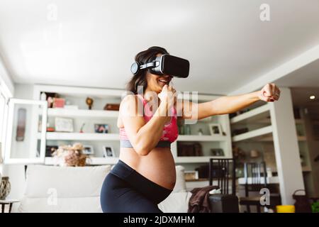 Donna incinta felice che indossa simulatore di realtà virtuale punzonatura a casa Foto Stock