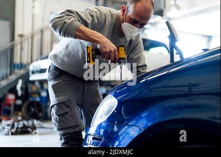 Meccanico automatico che lavora con cacciavite elettrico in garage Foto Stock