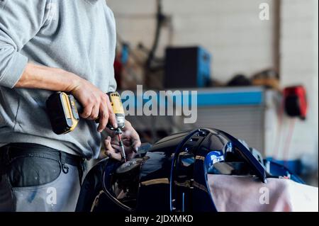 Le mani del meccanico che ripara la parte del veicolo con un cacciavite elettrico in officina Foto Stock