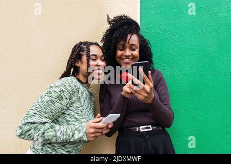 Felici amici multirazziali con telefoni cellulari in piedi di fronte al muro Foto Stock