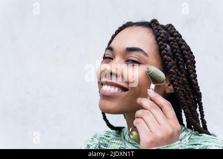 Donna sorridente con rullo di giada su sfondo bianco Foto Stock