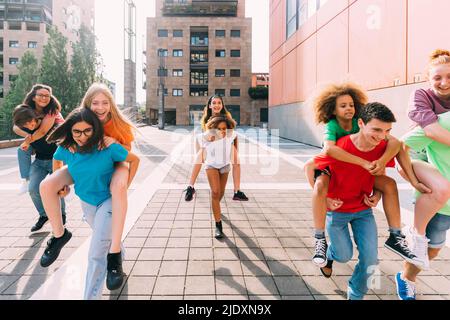 Ragazze e ragazzi felici che danno il giro di piggyback agli amici in giornata di sole Foto Stock