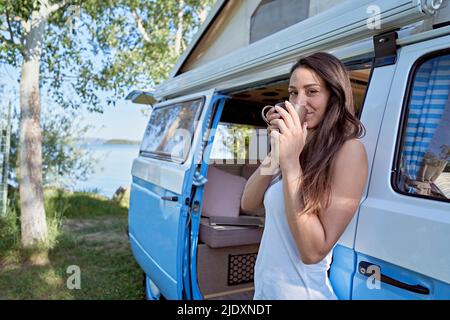 Donna che beve caffè alla porta del camper Foto Stock