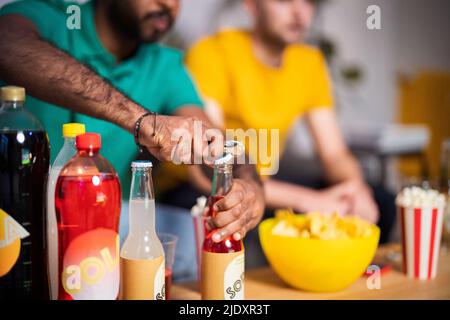 Mani di giovane uomo che aprono una bottiglia di bevanda a casa Foto Stock