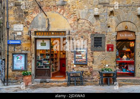Un pittoresco caffè con tavoli sul marciapiede di fronte al centro medievale della storica cittadina collinare di Volterra, in Italia, nella regione toscana. Foto Stock