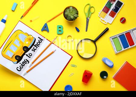 Set di cancelleria, taccuino con autobus disegnato e testo CHE VA A SCUOLA su sfondo giallo Foto Stock