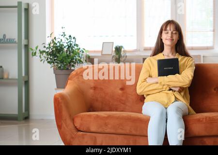 Ragazza adolescente con Sacra Bibbia seduta sul divano a casa Foto Stock