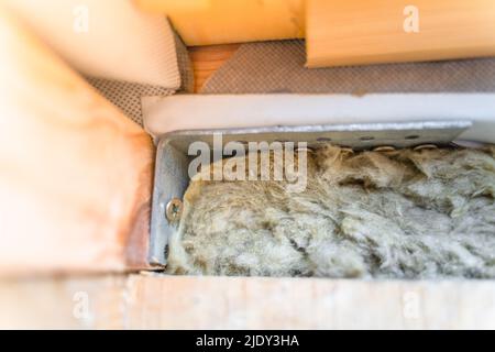 L'angolo rinforzato in acciaio fissa strutture in legno. Primo piano di un sottile strato di lana minerale tra l'idrobarriera e il rivestimento in legno Foto Stock