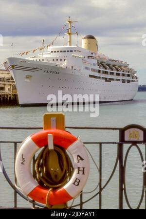 La nave da crociera TSS Fairstar ormeggiata nel Porto di Auckland, Nuova Zelanda nel 1984 dopo la crociera da Sydney, Australia. Originariamente una nave truppa britannica Oxfordshire fu convertita alla Fairstar di linea (Sitmar) e viaggiò tra l'Inghilterra e l'Australia fino al 1974 quando iniziò le crociere a tempo pieno del Sud Pacifico fino al suo viaggio finale nel 1997. In primo piano è un Auckland Harbour Board (AHB) anello vita (lifbuoy) attaccato ad una recinzione Foto Stock