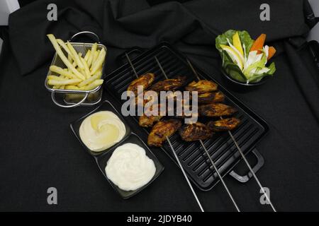 ali di pollo grigliate con patatine fritte e insalata di salsa su sfondo nero Foto Stock