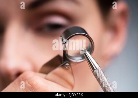 Primo piano della mano di un gioielliere femminile che guarda il diamante attraverso la lente d'ingrandimento Foto Stock