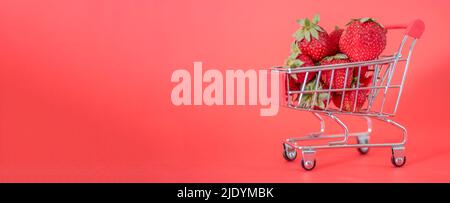 Carretto pieno di fragole fresche mature su sfondo rosso. Primo piano, vista laterale spazio. Grande sano e saporito concetto di negozio di bacche Foto Stock
