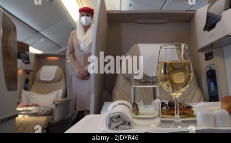 Un pasto di classe premium servito alla prima classe della compagnia aerea Emirates di Dubai, mentre l'assistente di volo che indossa la maschera facciale attende i passeggeri all'interno dell'aeromobile Boeing 777-300ER Foto Stock