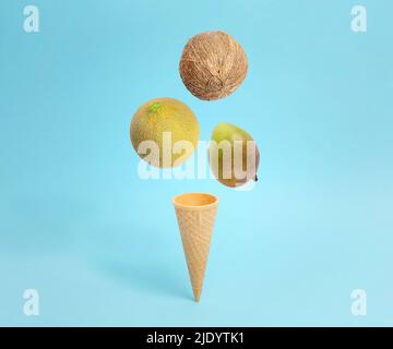 Cono gelato con cocco, melone e mango. Composizione concettuale creativa su blu pastello Foto Stock