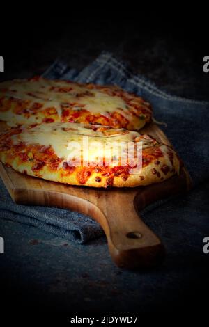 Pizza vegetale con formaggio fuso cotta su un tagliere di legno. Con un tovagliolo da tè su sfondo grunge. Foto Stock