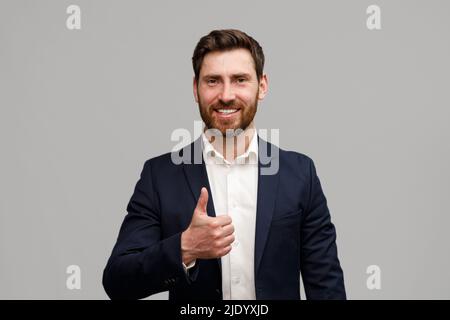 Ritratto di uomo d'affari sorridente cavalcando il pollice su sfondo grigio studio Foto Stock