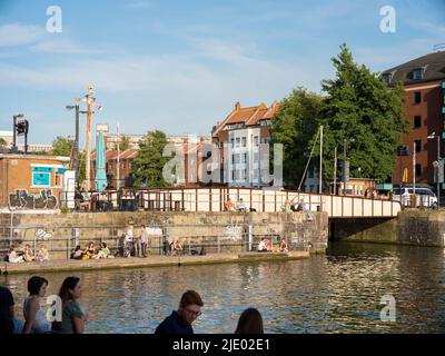 La gente si siede sul porto vicino all'Arnolfini e al Ponte dei principi a Bristol in una serata estiva soleggiata. Foto Stock