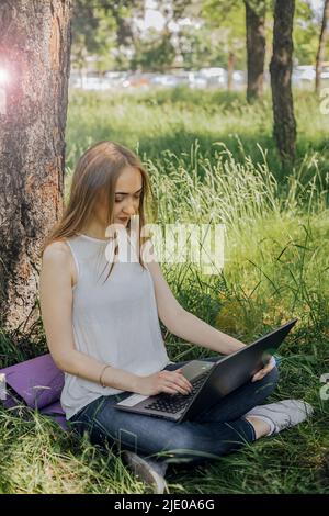 Sul banner, una giovane ragazza lavora con un computer portatile all'aria aperta nel parco, seduto sul prato. Il concetto di lavoro a distanza. Lavora come freelance. T Foto Stock