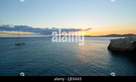 Luce del mattino, barca a vela, mare calmo, cielo azzurro, lunga nuvola grigio-blu, alba, alba rossastra, roccia tufa, rocce tufa, Spiaggia di Sarakiniko, MILOS Foto Stock