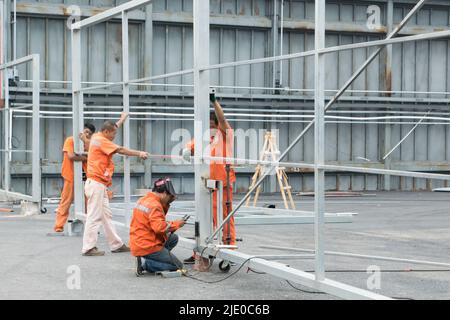 Un gruppo di lavoratori cinesi delle costruzioni lavora insieme per assemblare una struttura in acciaio di un hangar mediante saldatura di metalli. Centrale Pechino. Foto Stock