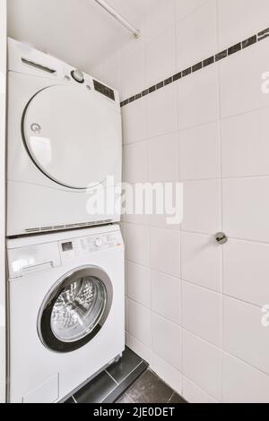 Armadio con lavatrice mechine in bagno piastrellato bianco con wc appeso alla parete Foto Stock