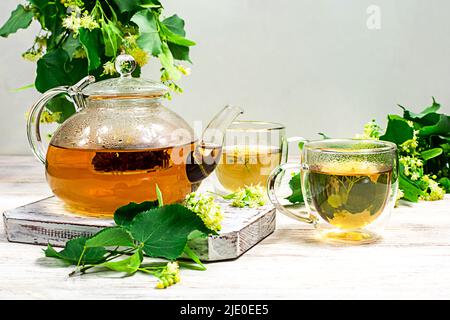 Teiera e due tazze di tè con un tiglio su un tavolo di legno. Tè healing. Foto Stock